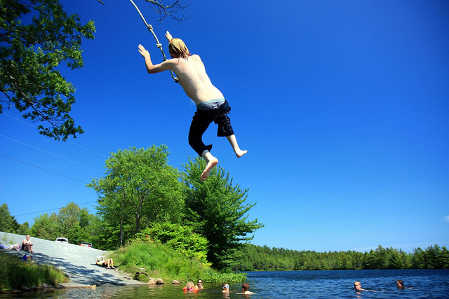 Teen boy jumping off rope swing over water